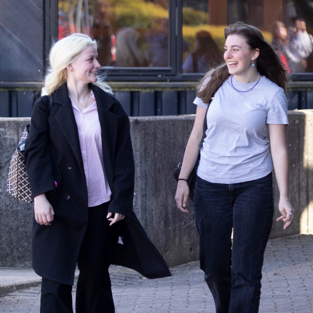 To elever fra Campus Odsherred går ude foran skolen. Pigerne smiler til hinanden.